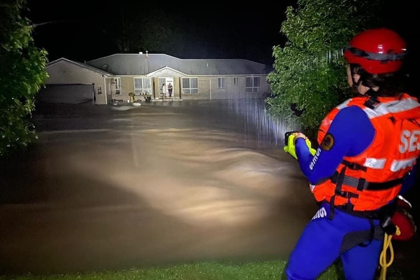 SES volunteer shines flashlight across floodwater onto a house.