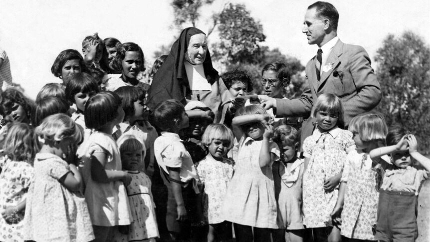 Black and white photo of aboriginal children with a nun and man in a suit