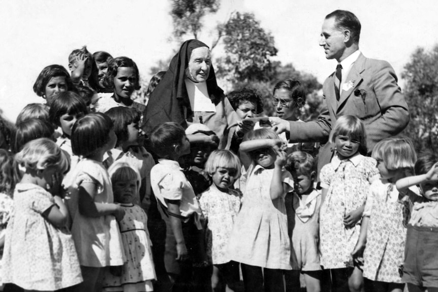 Black and white photo of aboriginal children with a nun and man in a suit