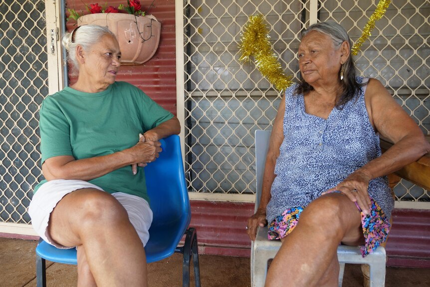 two indigenous residents chat on chairs outside a house