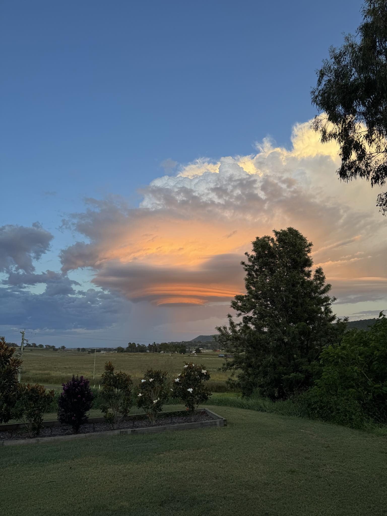 An orange and white funnel-shaped cloud in a blue sky above a rural landscape.