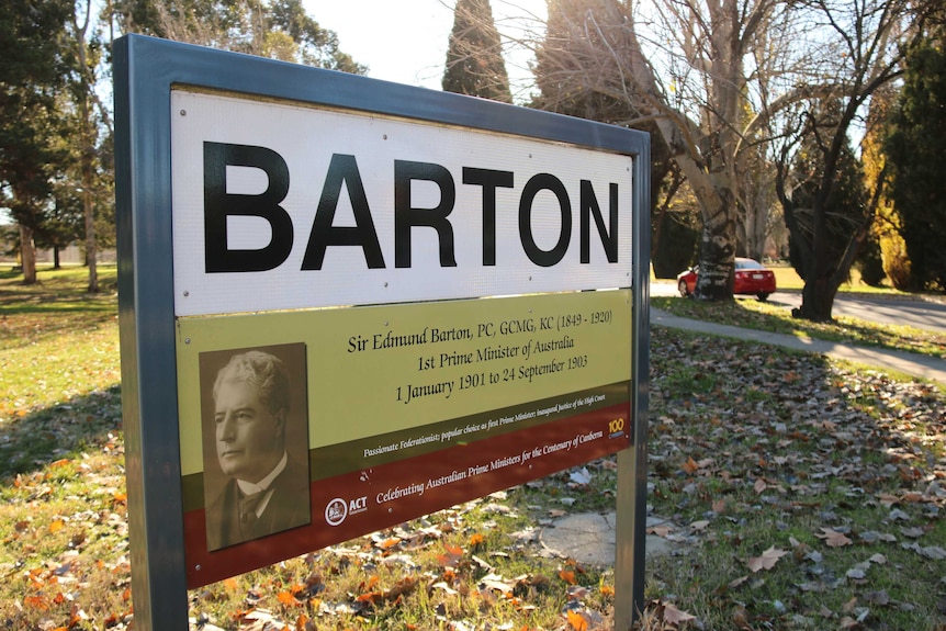 A sign in a grass field that reads "Barton" with an image of Edmund Barton and details of his life and death.