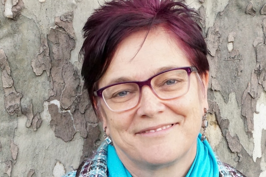 Pip Brennan who has short red hair and glasses smiles at the camera in front of wall