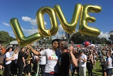 Two men kiss under gold ballons spelling out "LOVE"
