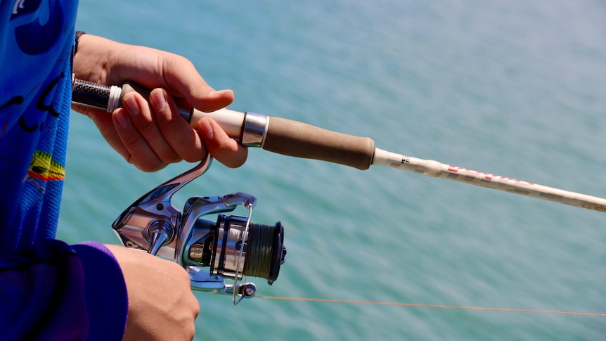 A person holds a fishing rod. There is blue ocean in the background