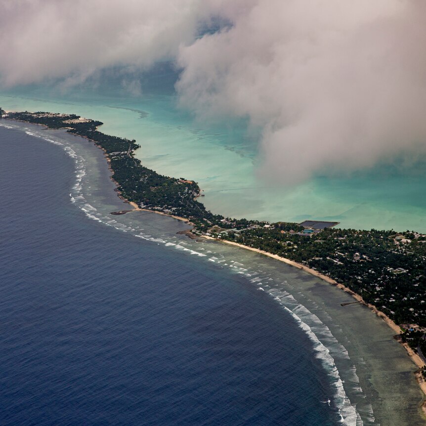 An aerial view of the Pacific Island of Kiribati, surrounded by turquoise water and a wisp of cloud.
