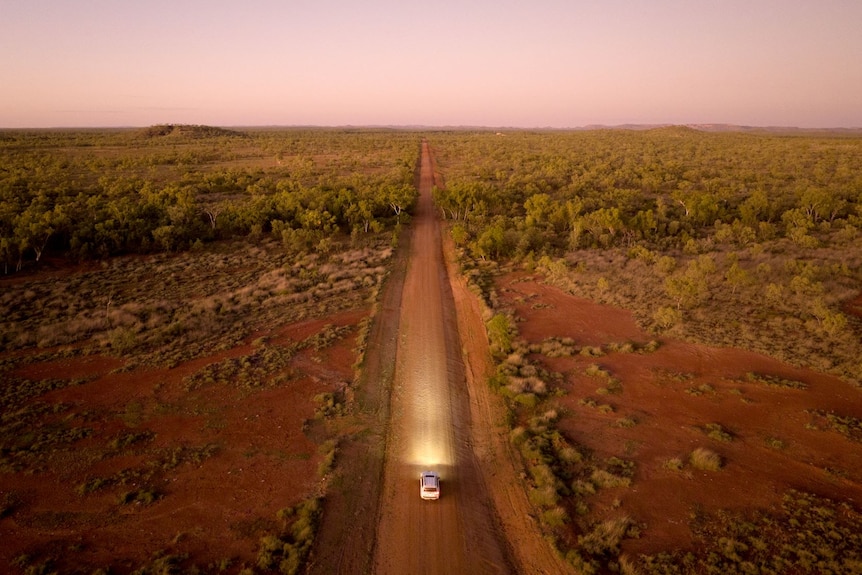 A single car drives on a red, dirt road in outback Queensland