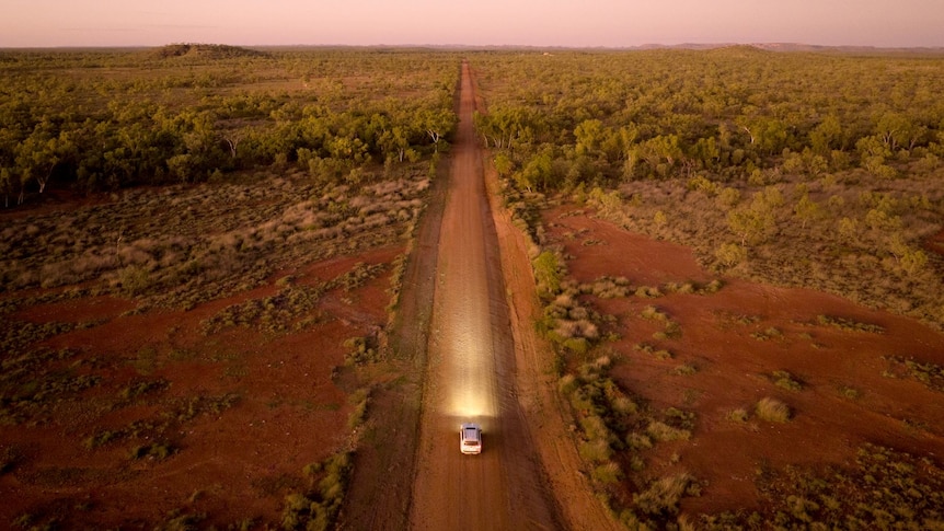 A single car drives on a red, dirt road in outback Queensland