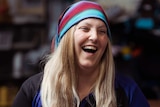 A head and shoulders shot of a laughing Dee Freitag wearing a black and purple shirt and a striped head scarf.