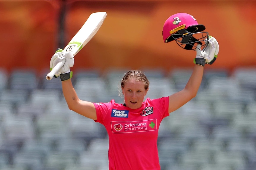 A Sydney Sixers WBBL player holds her bat in one hand and her helmet in the other as she celebrates a century against the Stars.