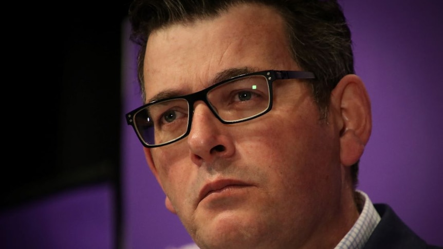 A close-up of a man with short black hair and black-rimmed glasses looking serious.