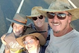 A family of four in akubra hats and sunglasses smile at the camera
