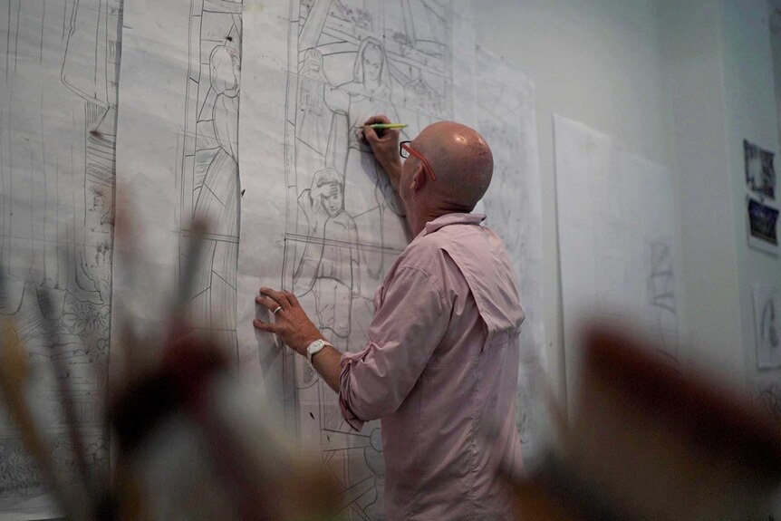 A man sketches cartoons on a large sheet of paper stuck to a wall