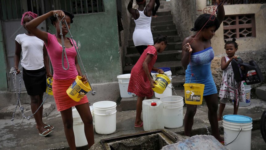 Women pull water out of a well using plastic buckets.