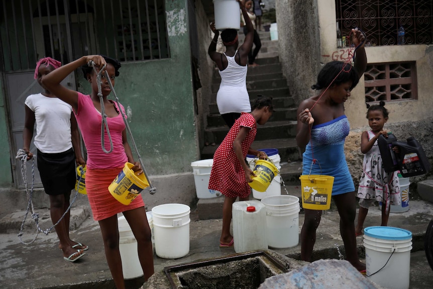 Women pull water out of a well using plastic buckets.