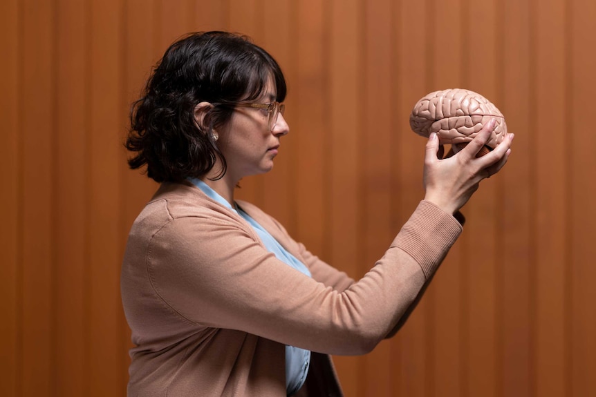 Daniela holds up a model of the brain, staring at it.