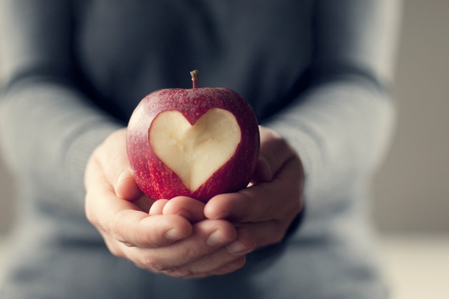 Someone holding an apple with a heart shape cut out of it