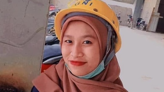 A woman wearing a yellow helmet smiles, while looking at the camera.