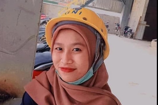 A woman wearing a yellow helmet smiles, while looking at the camera.