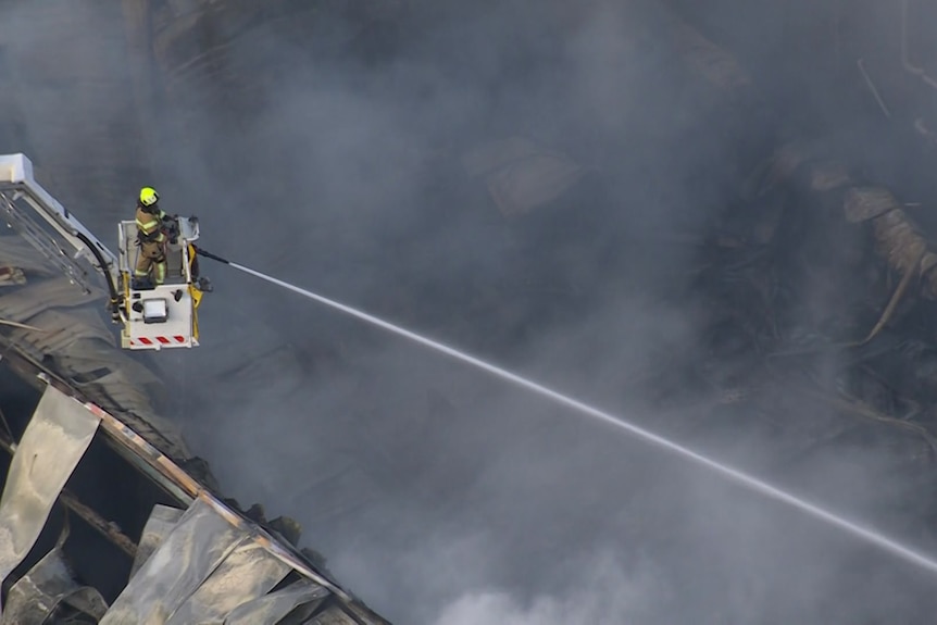 A fireman in a cherry picker aims a stream of water at the site of a factory fire