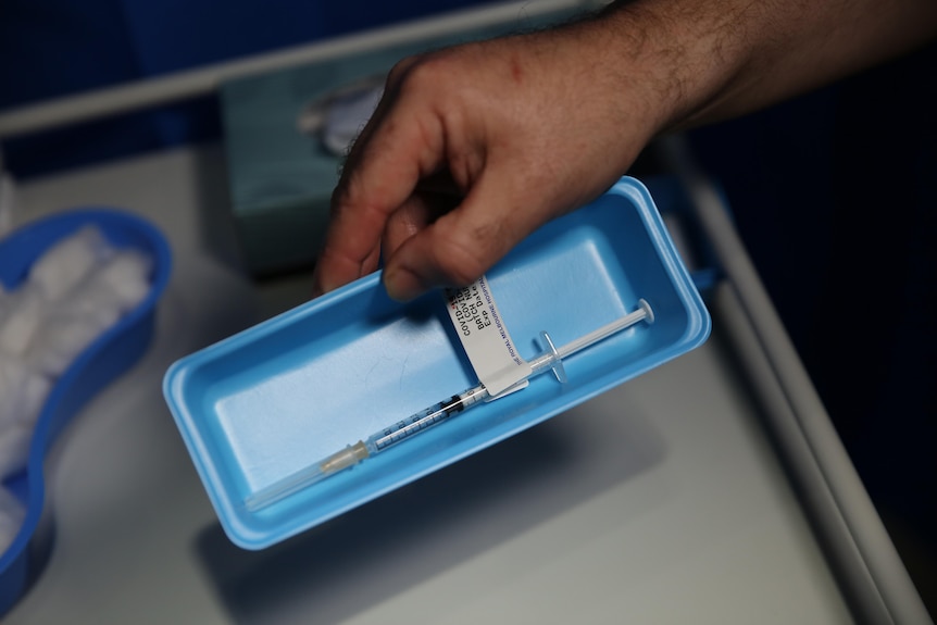 A male hand holds a blue plastic box containing a COVID vaccine.