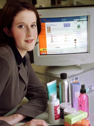 Woman standing next to an old computer with beauty products in front of her.