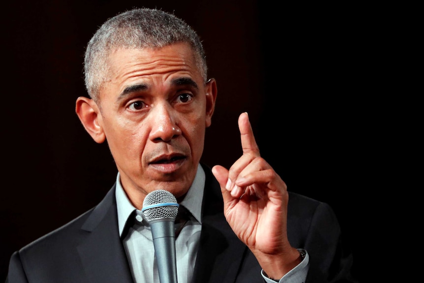 Barack Obama points his left index finger while speaking into a microphone.