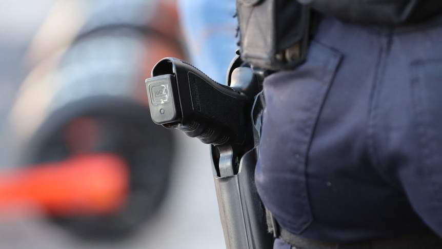 Close up of Queensland Police Service-issued black gun in holster on navy pants