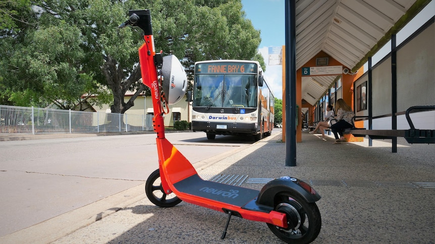 A bright orange scooter at a bus stop with a number 6 bus to Fannie Bay in background.