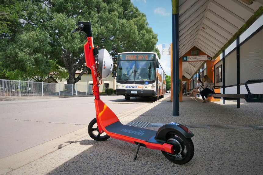 A bright orange scooter at a bus stop with a number 6 bus to Fannie Bay in background.