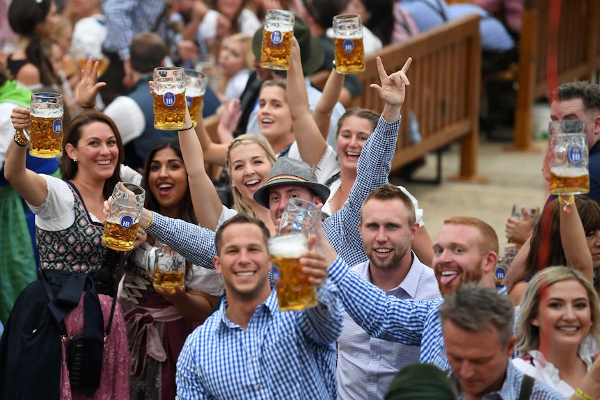 Men an women in checked shirts and traditional German dresses raise large glasses full of beer.