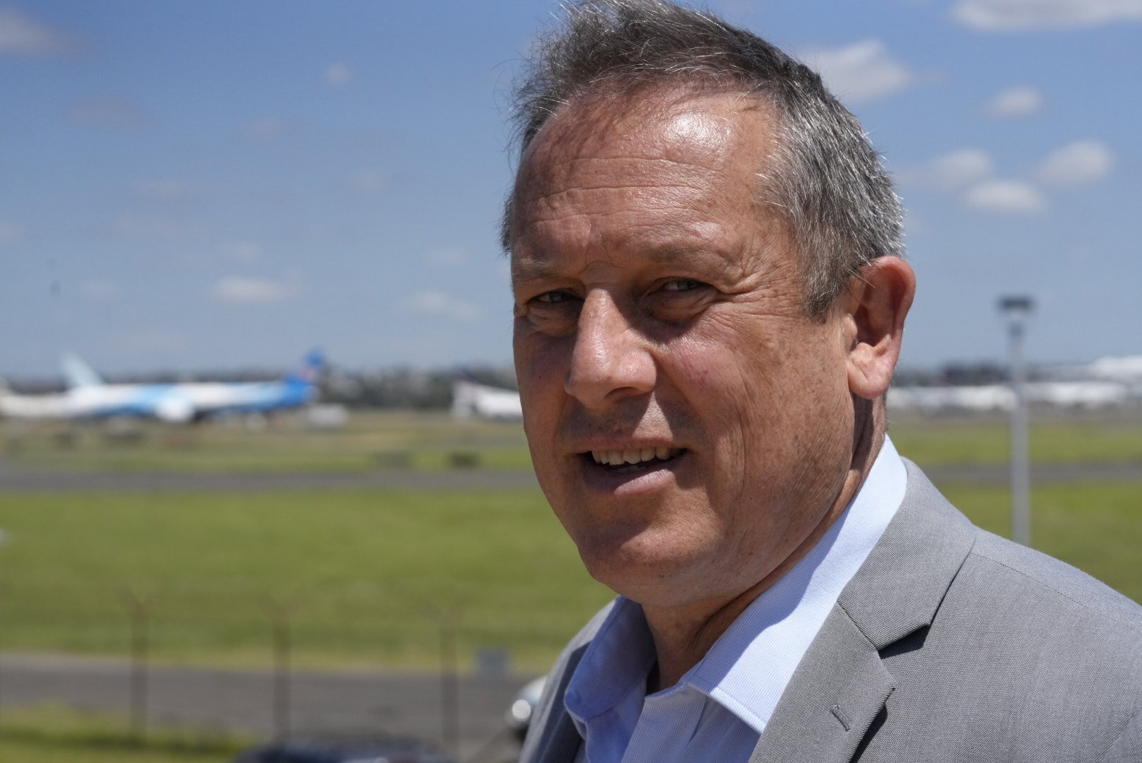 Man wearing a grey suit, with a plane runway in the background.