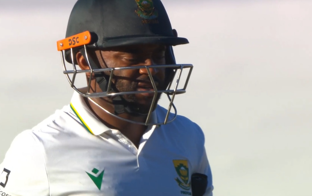 Bavuma looks down with a disappointed expression wearing cricket helmet and visor.