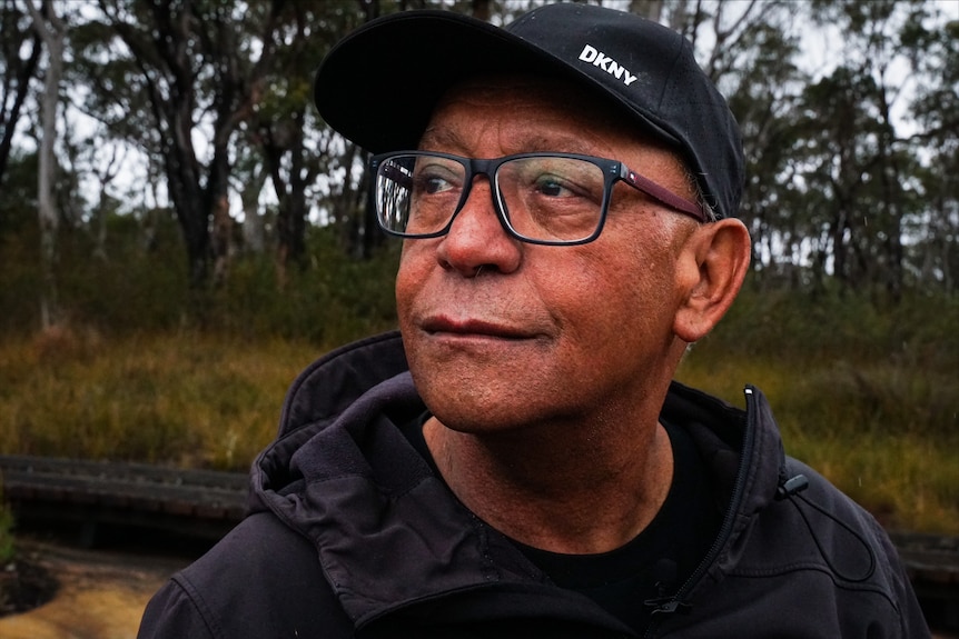 An Aboriginal man with glasses looking out in the distance in the bush.
