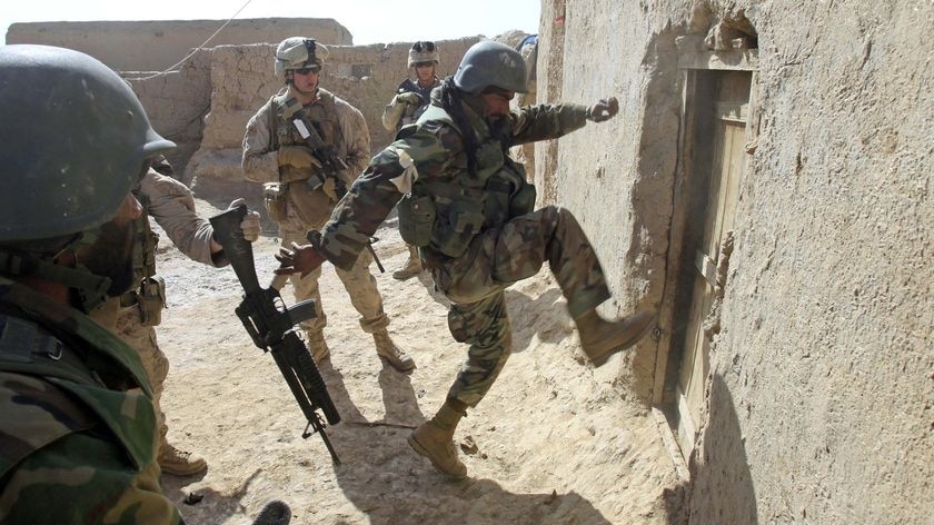An Afghan soldier attempts to break open a door as US Marines look on