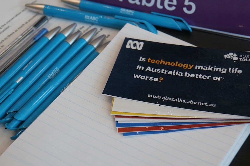 Pens, paper and a card asking "Is technology making life in Australia better or worse?" sit on a table.