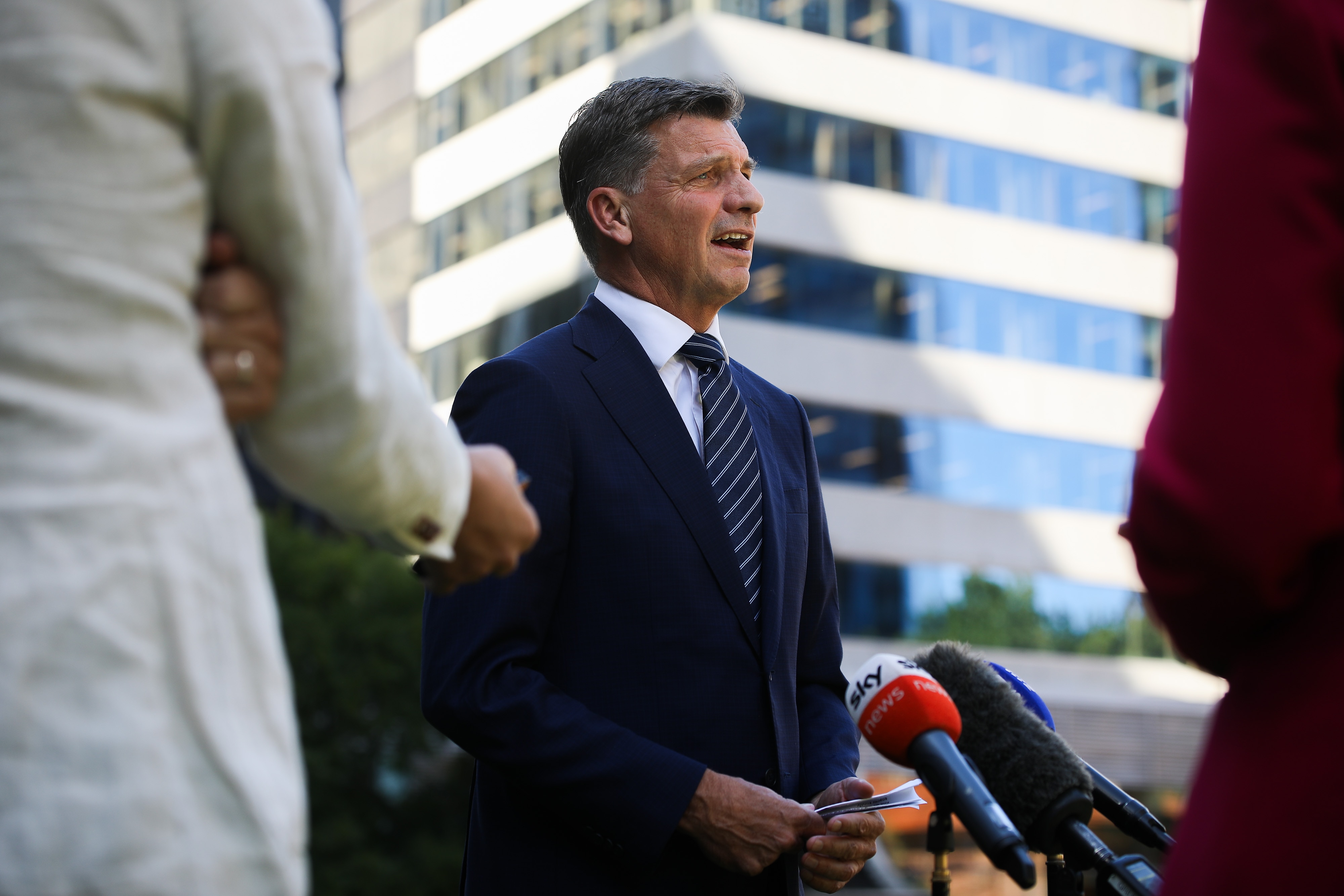Una toma intermedia del líder de la oposición federal, Angus Taylor, vestido con traje y corbata, hablando por micrófonos en una puerta afuera.