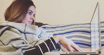 Writer Stephanie Coombes lying on her couch, typing on her laptop.