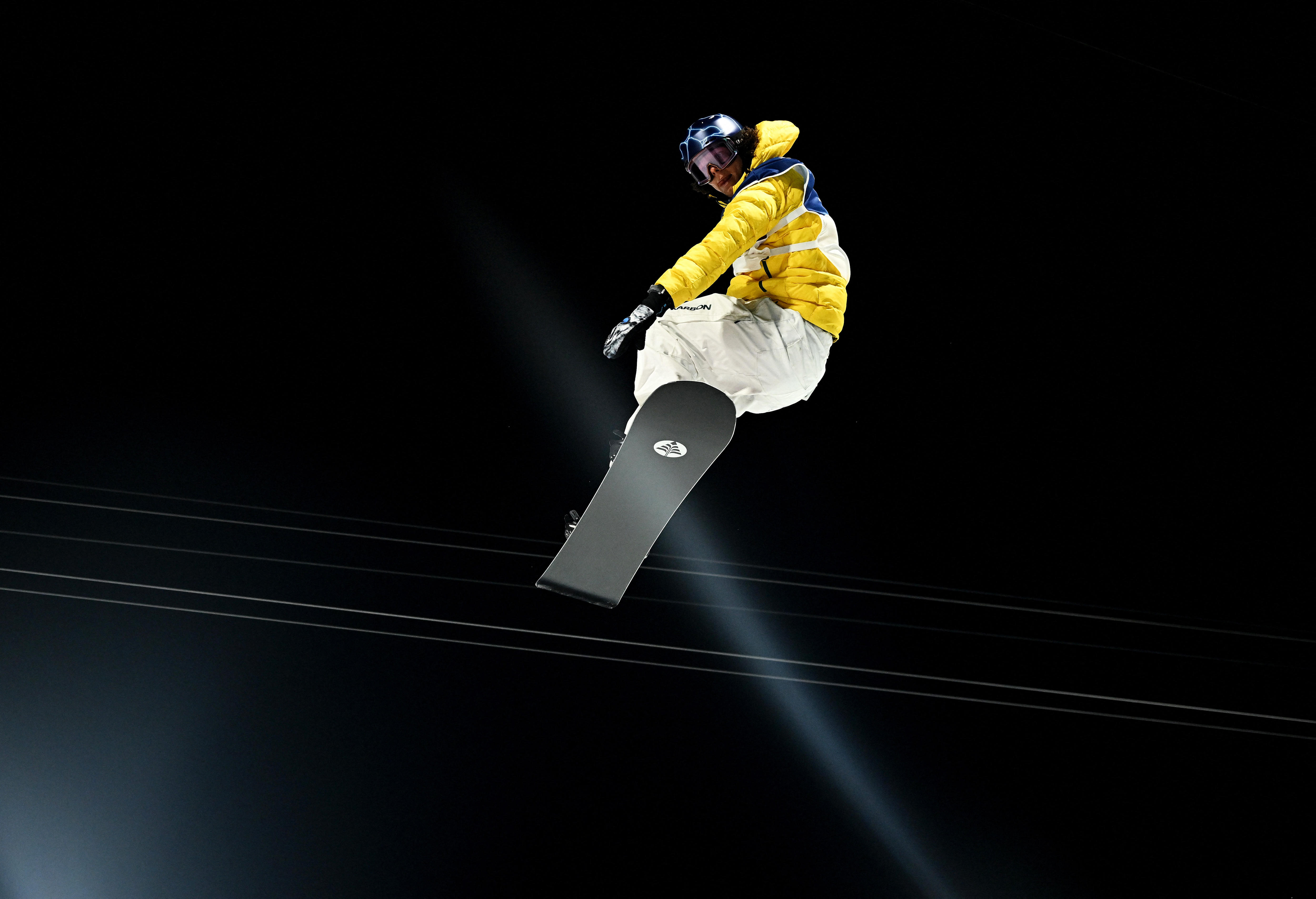 An Olympic snowboarder flies through the air during a competition at night.