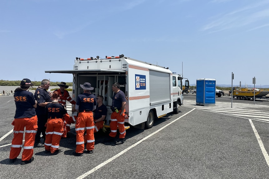 Several SES personnel standing at the back of an SES truck at a boat ramp near a body of water