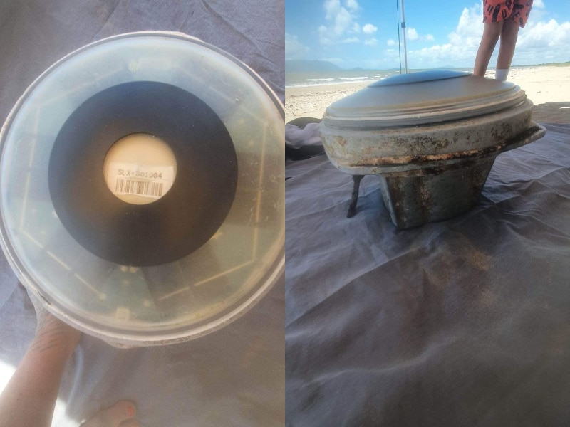 A round plastic device with a serial number and solar panels on a beach.