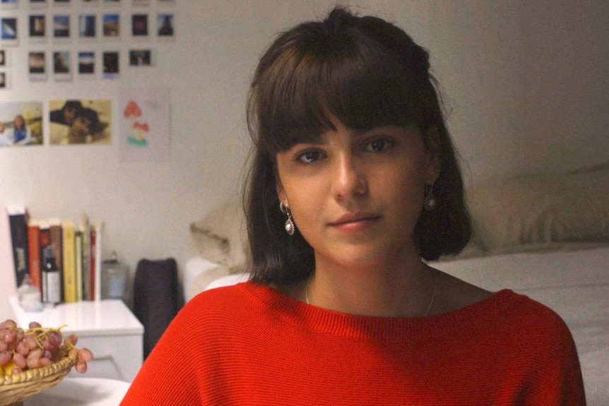 Tight shot of Anna in bedroom looking to camera with sad face.