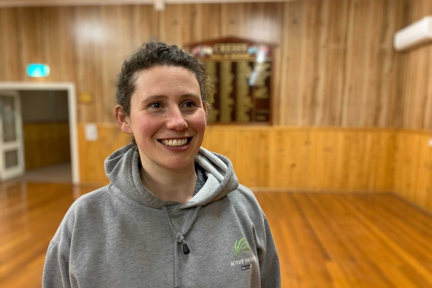 A young woman in a grey hoodie top smiles in a gym