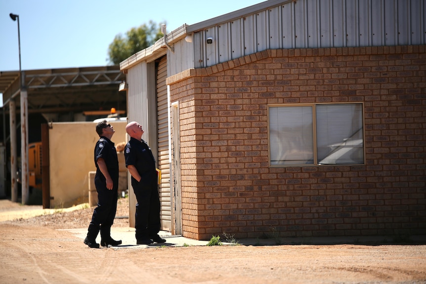 Two police in dark blue uniforms stare up at a CCTV camera.