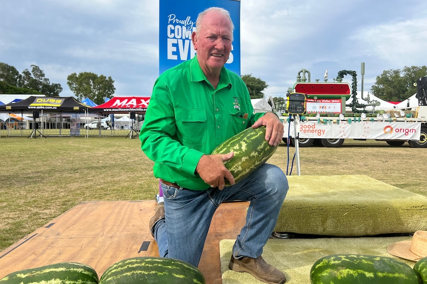 A man crouches down while holding a watermelon.
