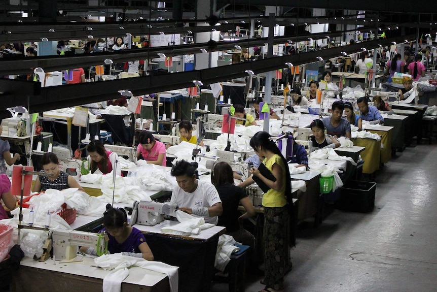 Workers sit at tables sewing clothes.