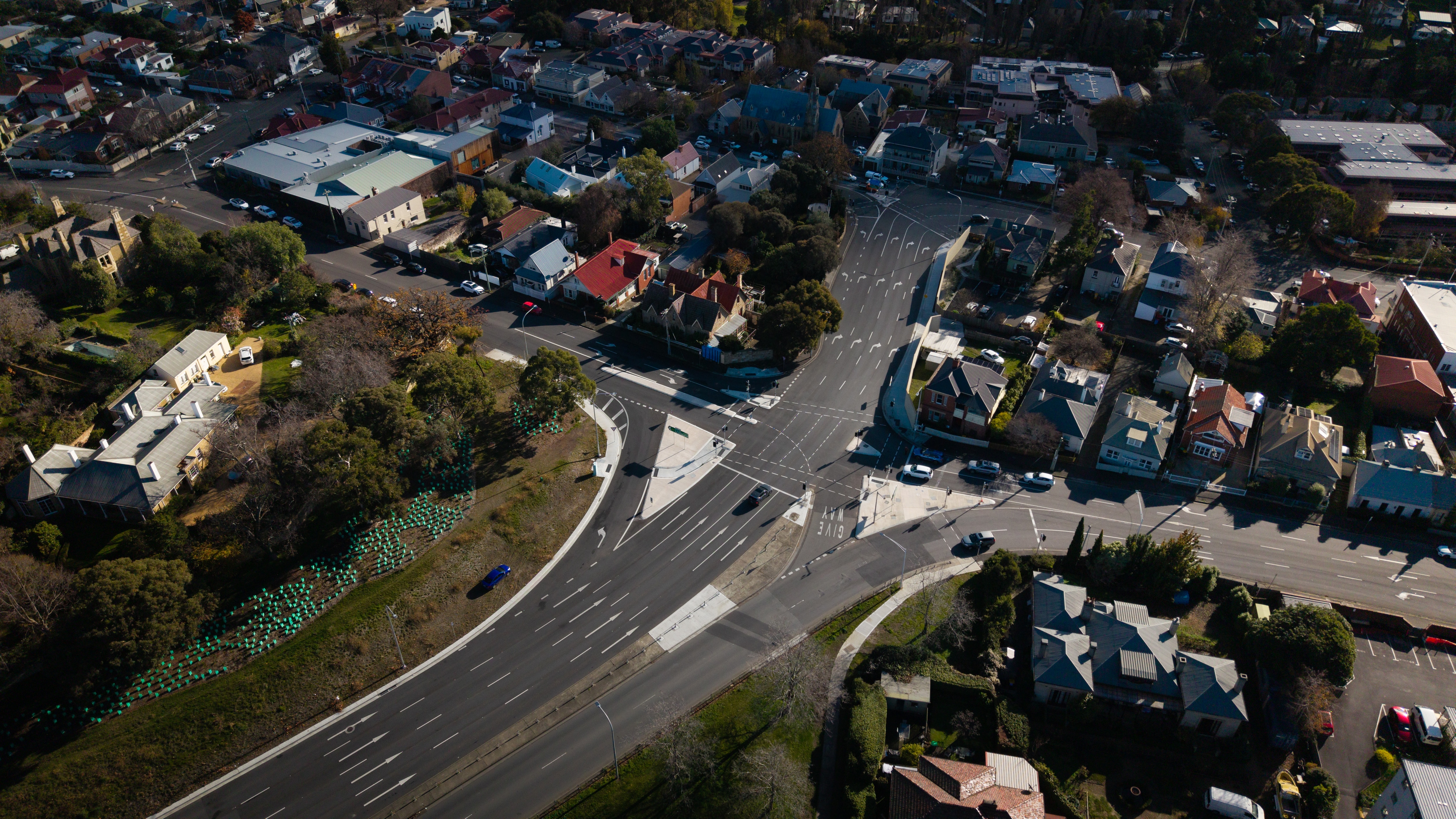 Aerial shot of a long road with busy traffic, winding through a hilly suburban neighbourhood