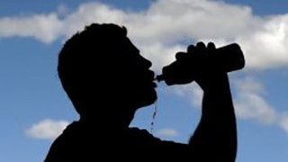 A sportsman takes a drink silhouetted against a blue sky with clouds in it.
