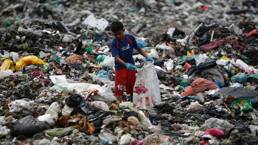 A boy, surrounded by a pile of trash, scavenges for plastic for recycling at a garbage dump site.