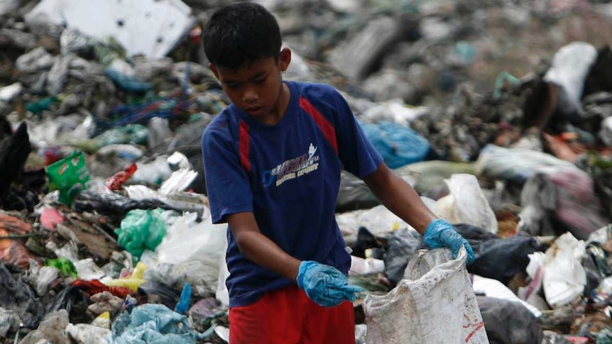 A boy, surrounded by a pile of trash, scavenges for plastic for recycling at a garbage dump site.